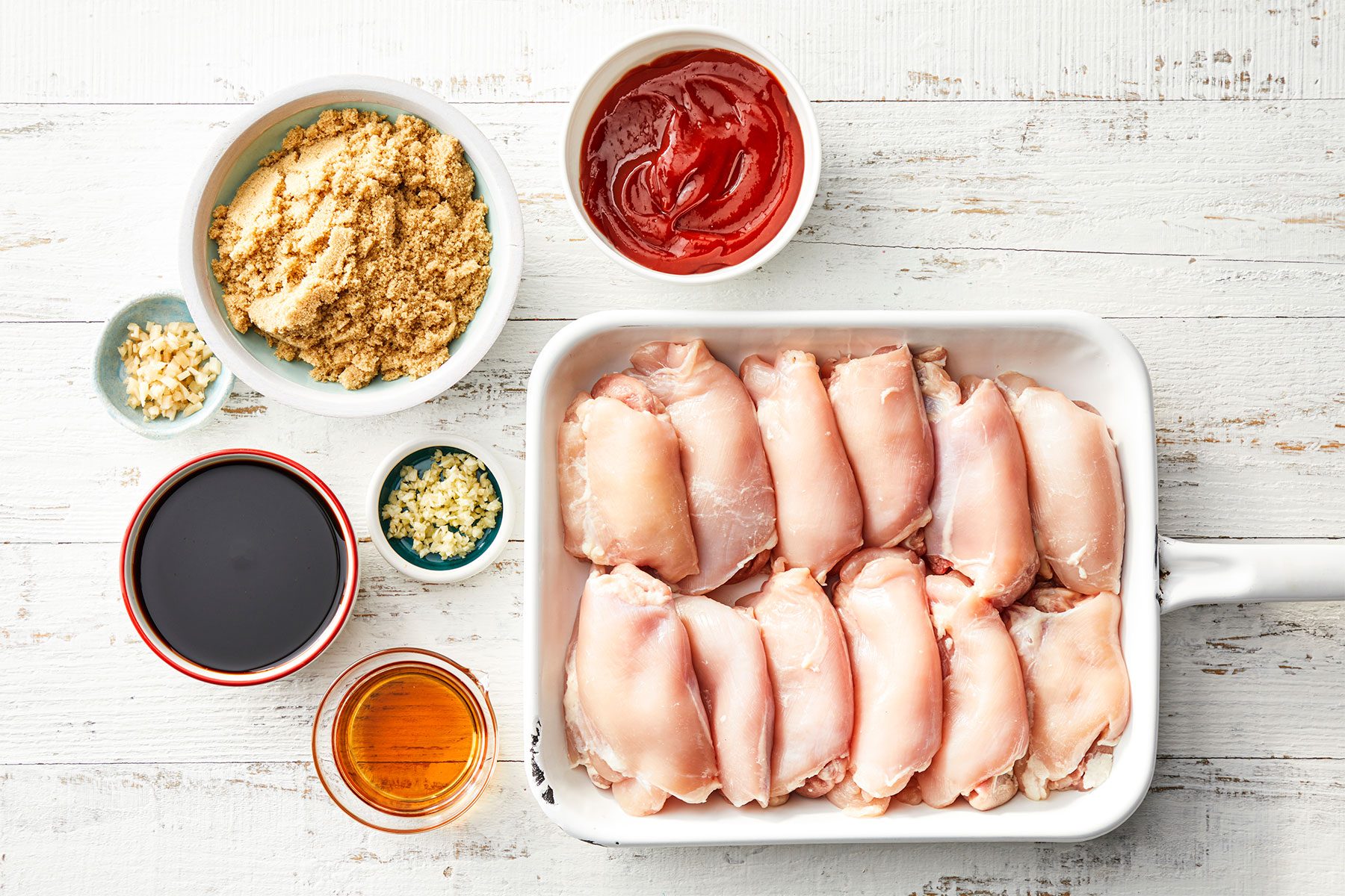 Overhead shot of 12 chicken thighs and other ingredients; white wooden background;