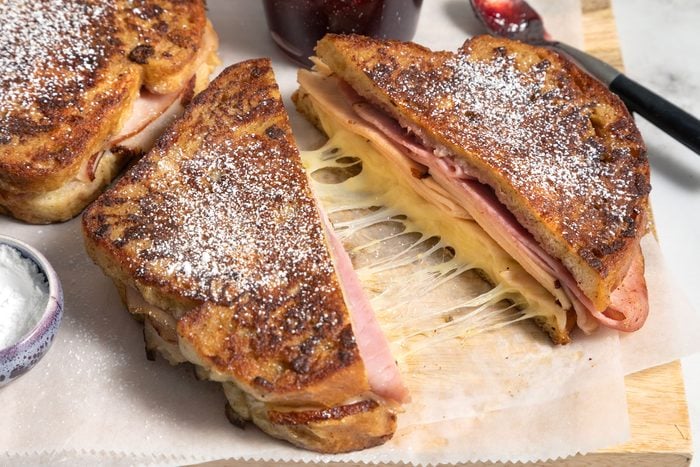 Monte Cristo Sandwich served on wooden board with jar of jam on the side