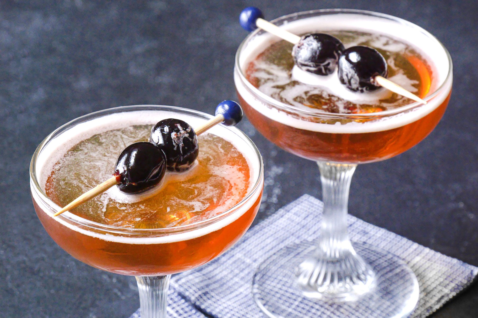 Two Rob Roy cocktails garnished with cherries served in elegant glasses