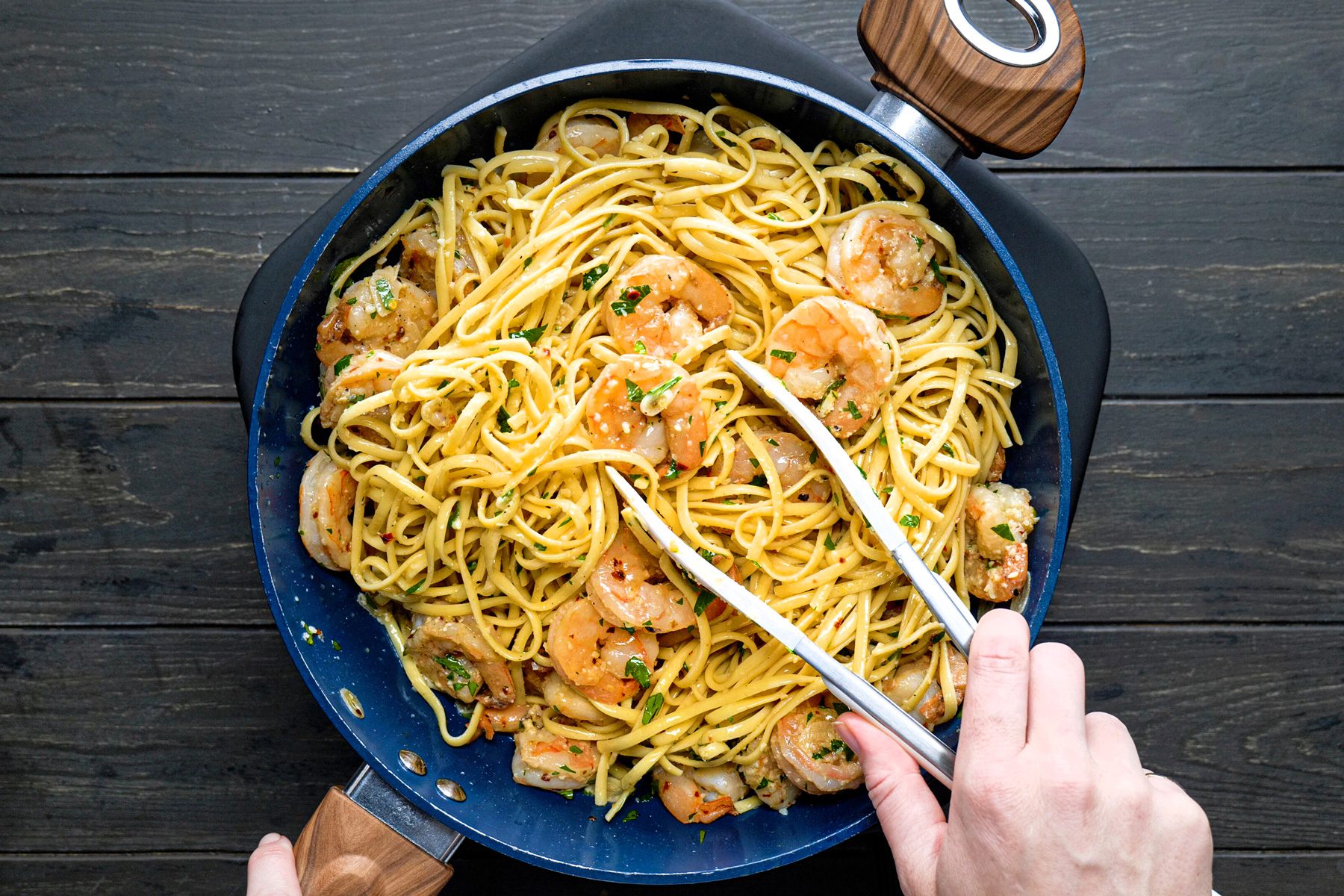 A person holding tongs to a bowl of pasta with shrimp