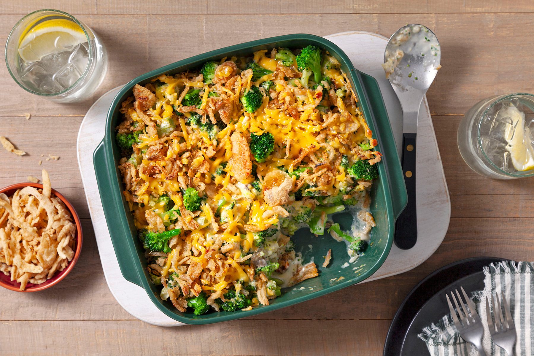 Cheesy Cheddar Broccoli Casserole in a Green Dish Next to a Serving Spoon on a Table