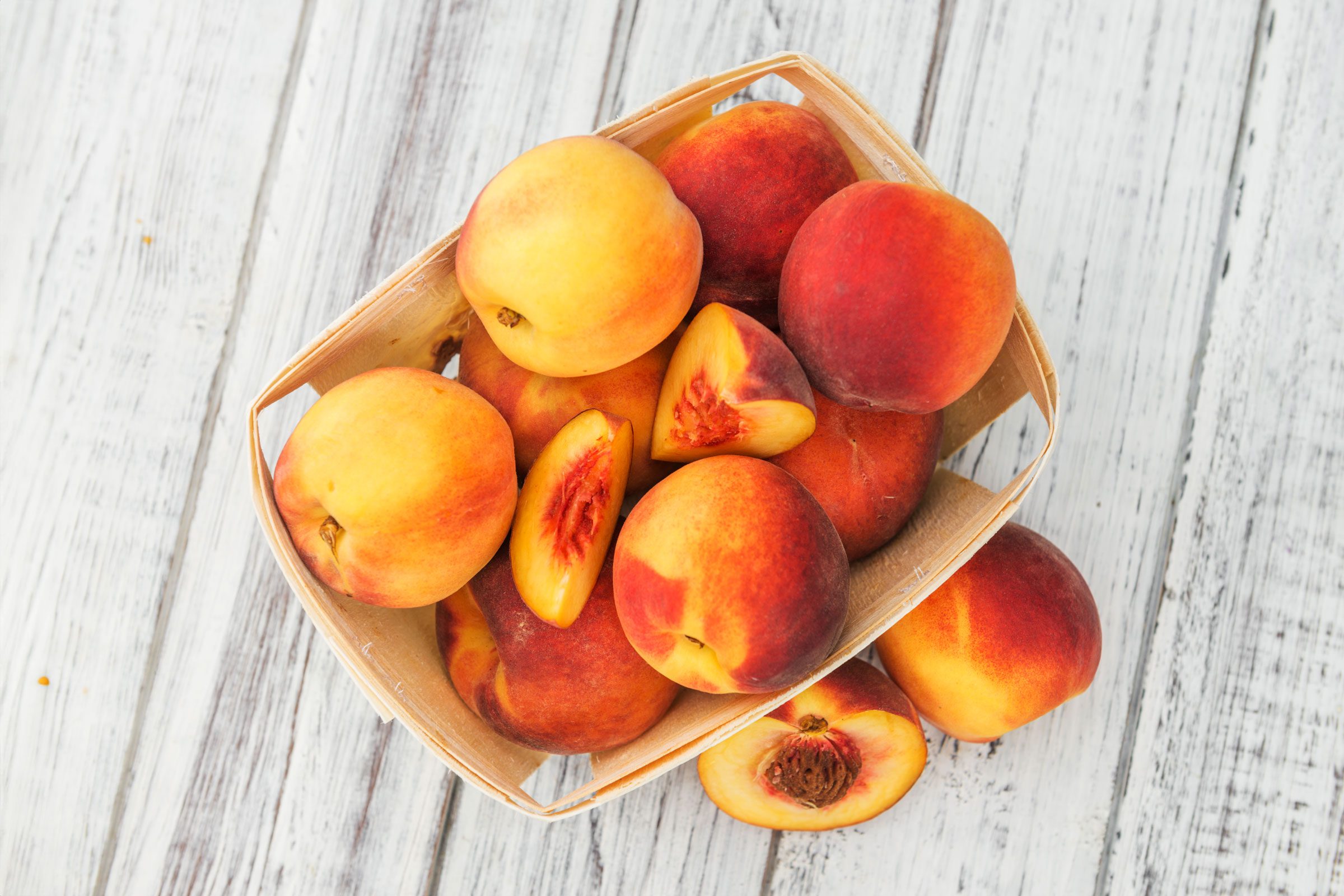 peaches in a wooden container on white wood surface