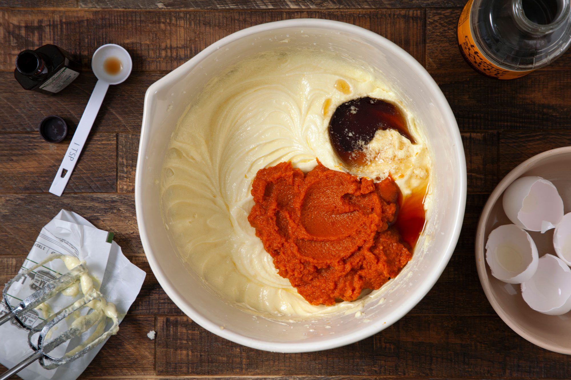 overhead shot of creamed butter, pumpkin puree, maple syrup and vanilla in a large bowl on wooden surface