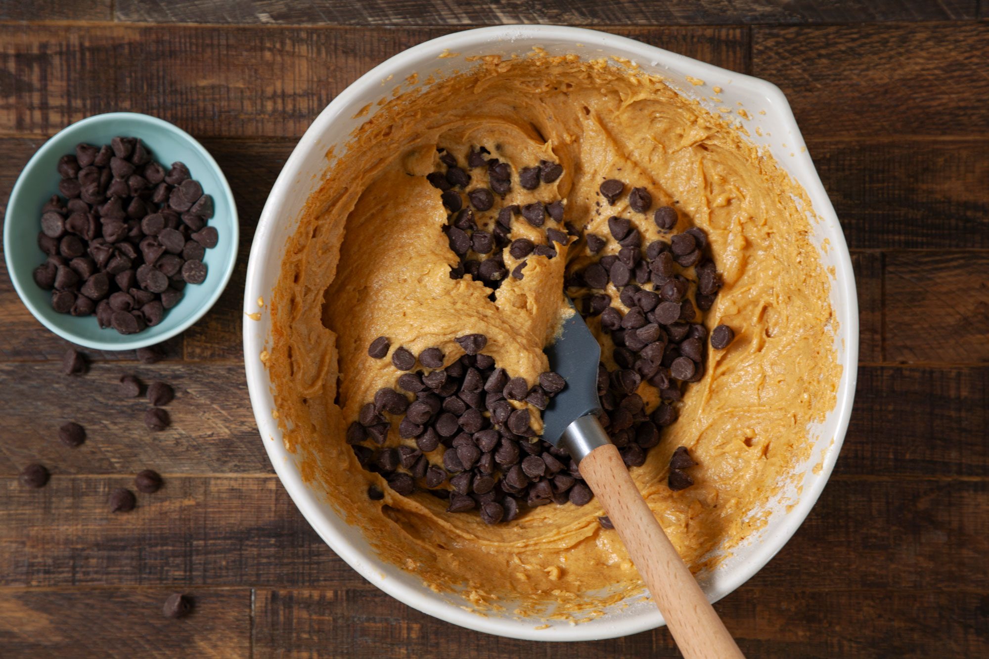 overhead shot of Pumpkin Bars batter, chocolate chips and spatula in a large bowl on wooden surface