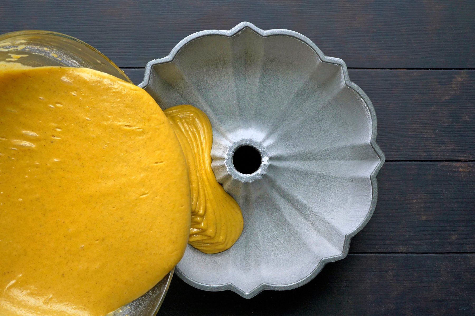 A person pouring pumpkin bundt batter into fluted tube pan