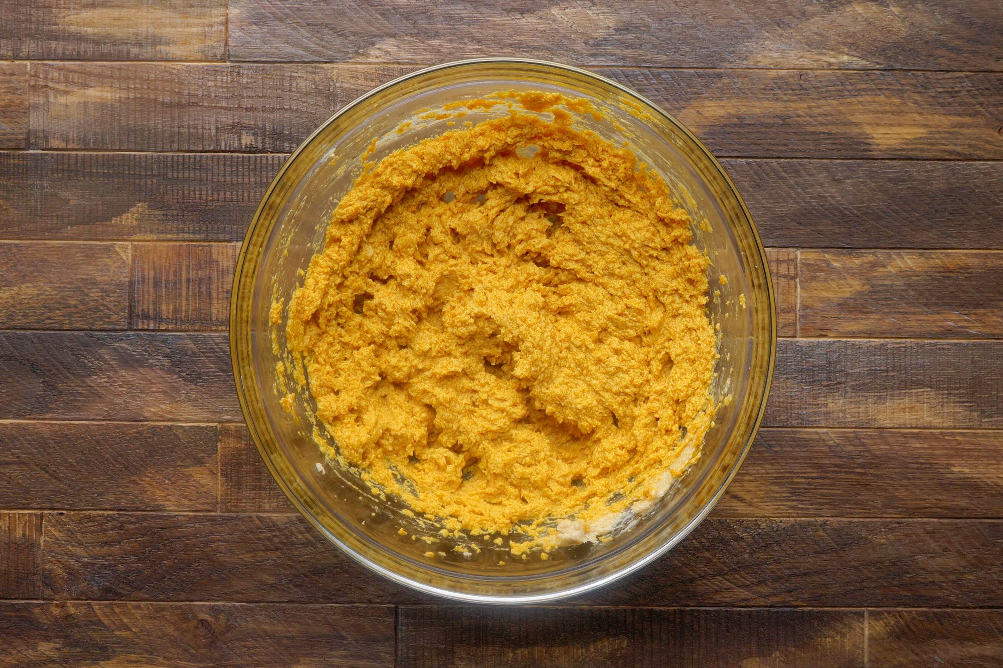 overhead shot of pumpkin cookie batter in a large glass bowl on wooden surface