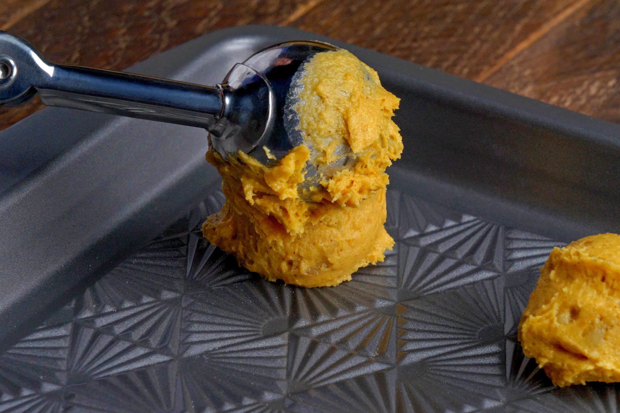 Dropping a scoop of pumpkin cookie dough onto a greased baking sheet