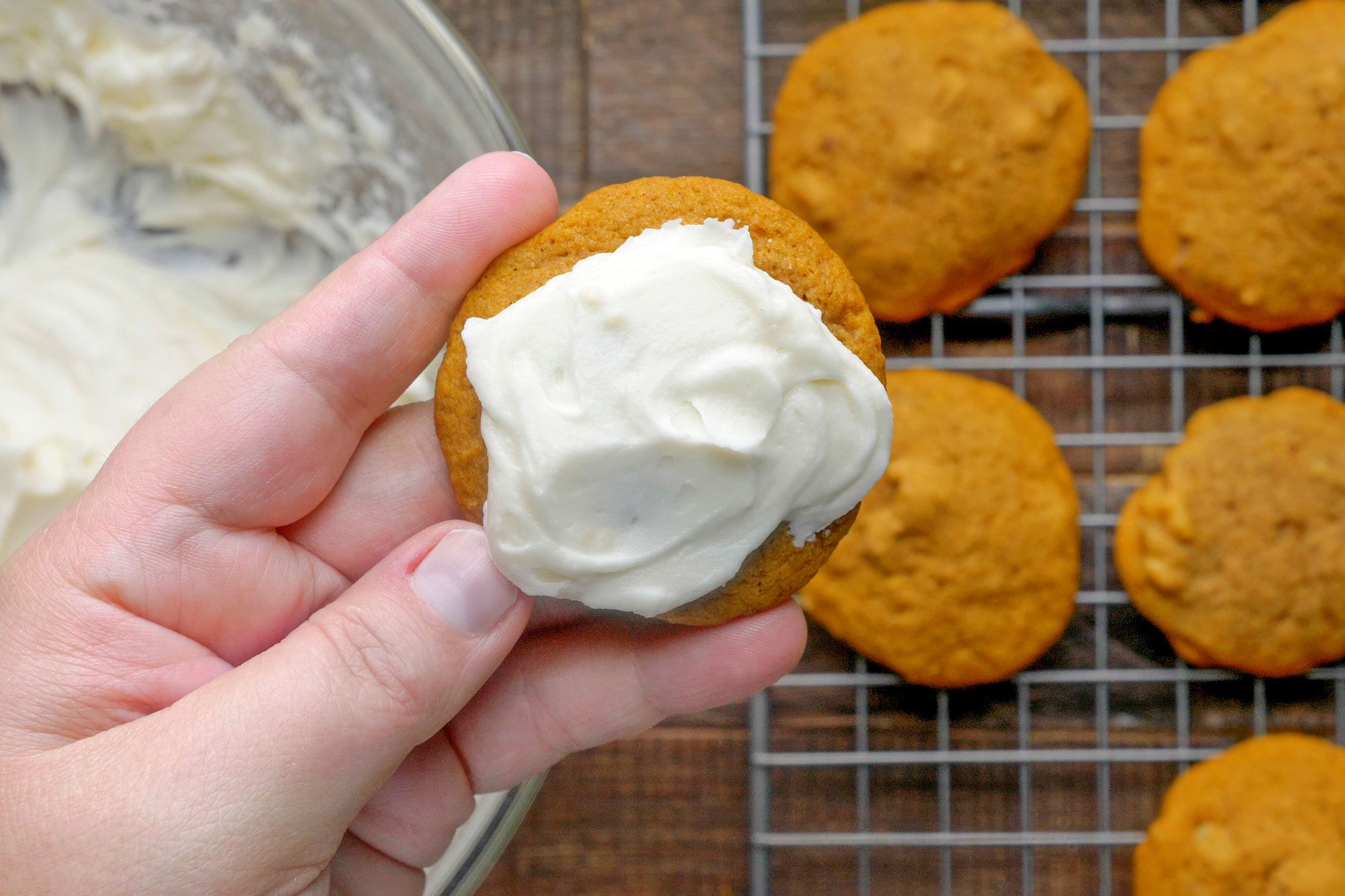 overhead shot of a hand holding Pumpkin Cookie With Cream Cheese Frosting