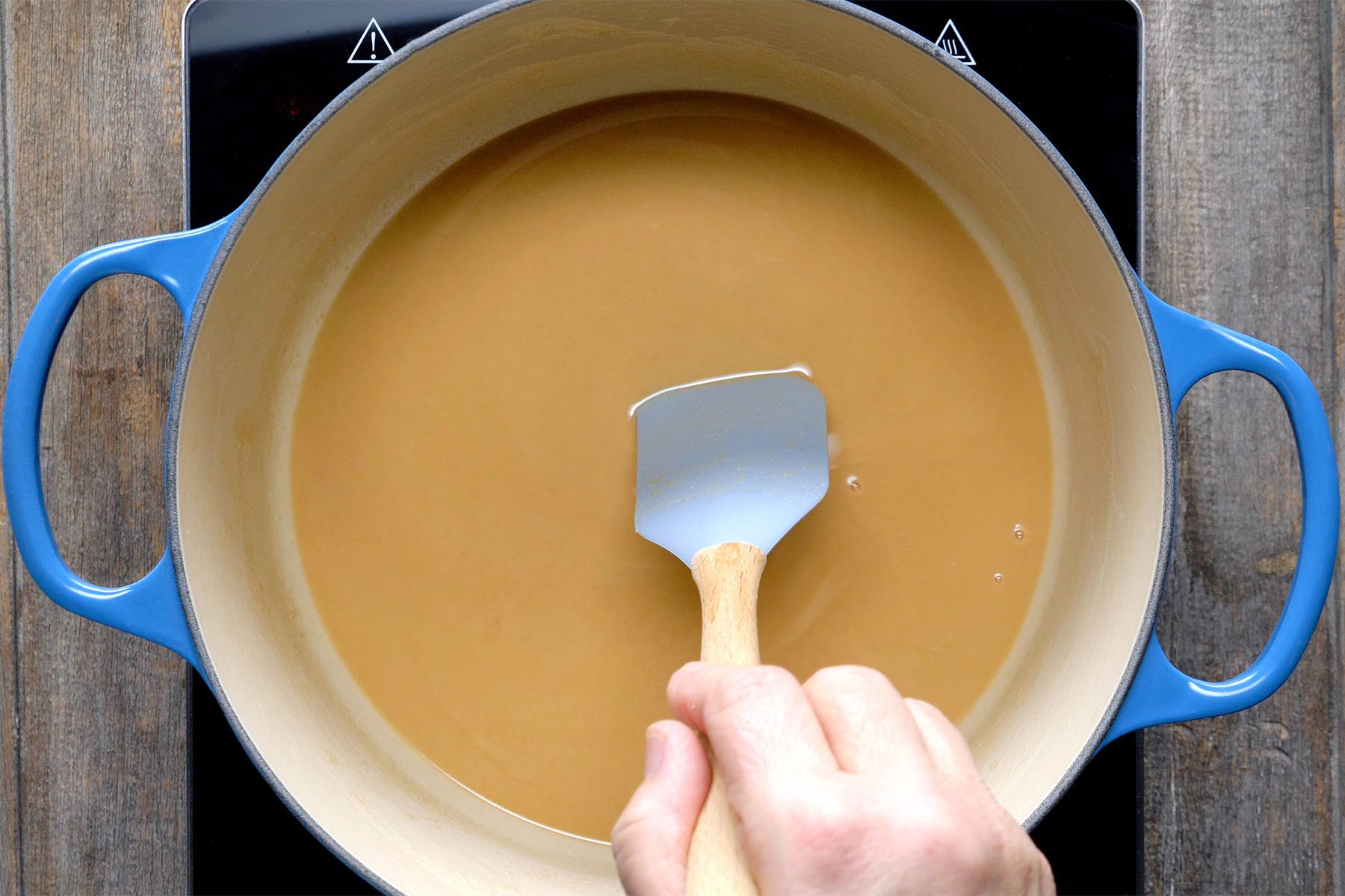Overhead shot of a heavy Dutch oven; combined flour and oil until smooth; cook over medium-high heat for 5 minutes; stirring constantly; spatula; wooden background;