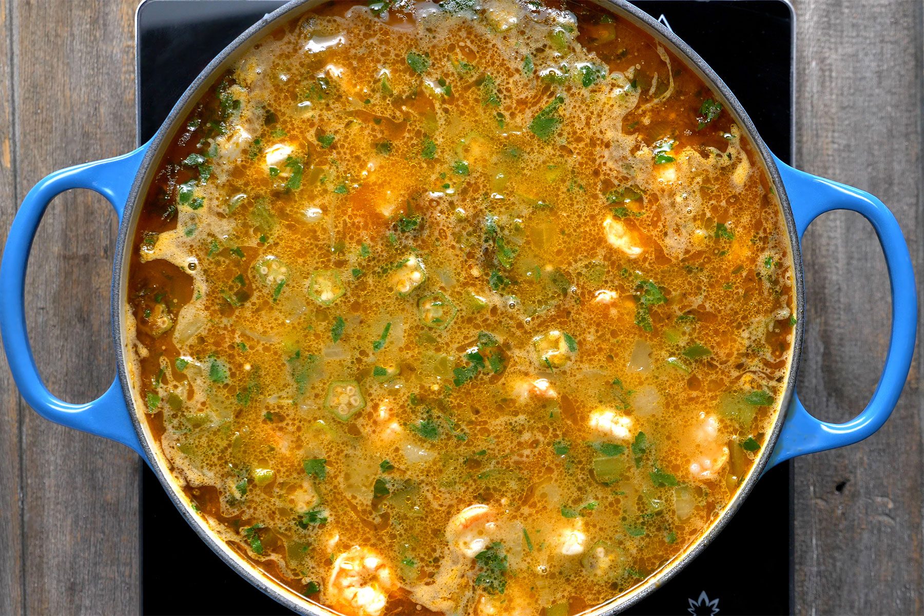 Overhead shot of added shrimp and parsley; Simmer; uncovered; about 5 minutes more or until seafood is done; remove from heat; stir in Cajun seasoning; wooden background;
